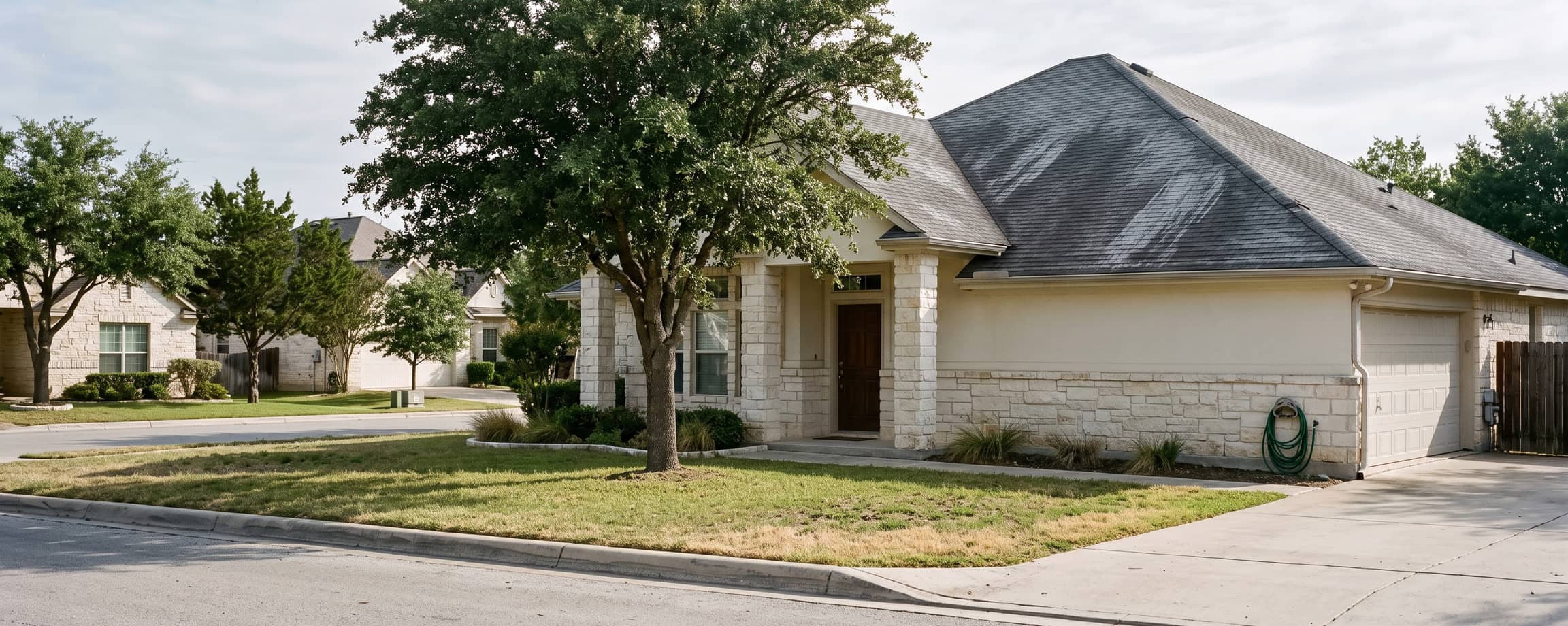A Central Texas limestone ranch house seen from the street with its original worn dark grey shingle roof, before any work has started