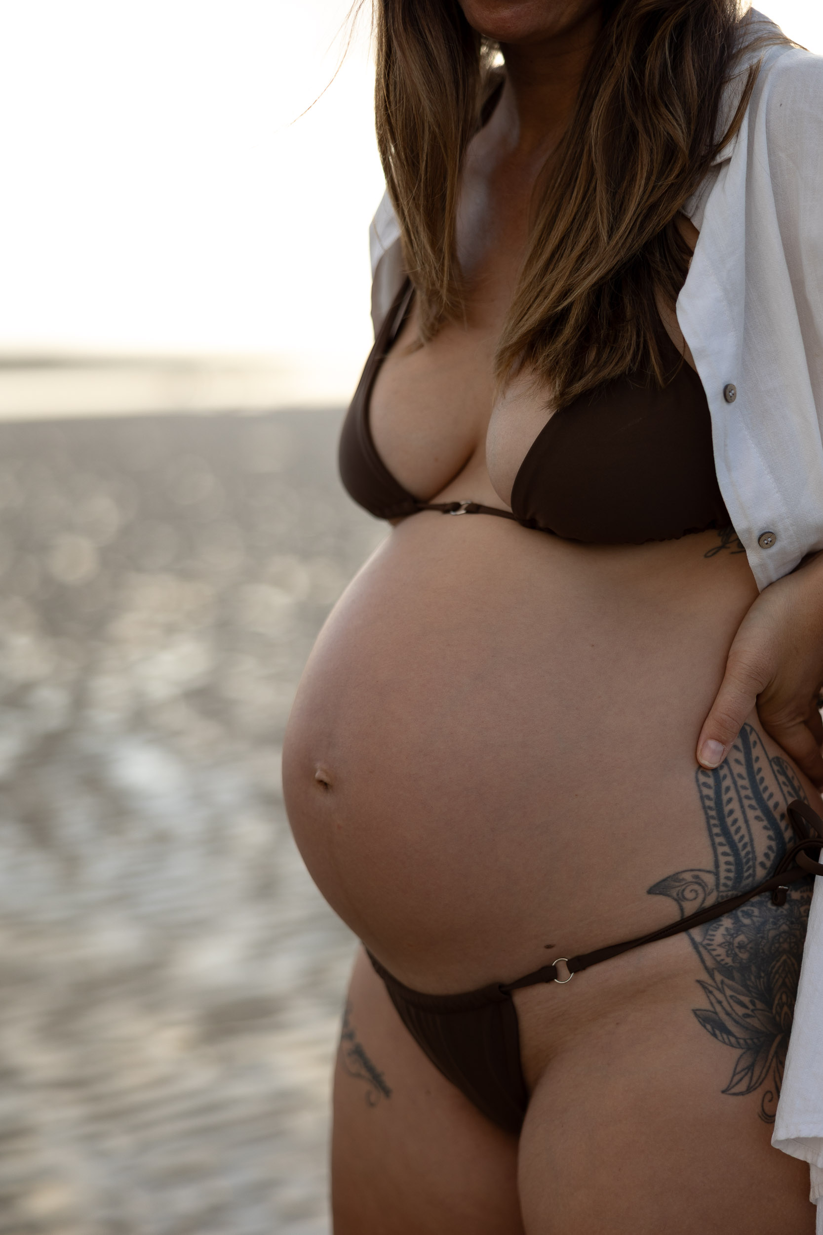 Pregnant woman standing barefoot on Mackay beach at sunrise during maternity session