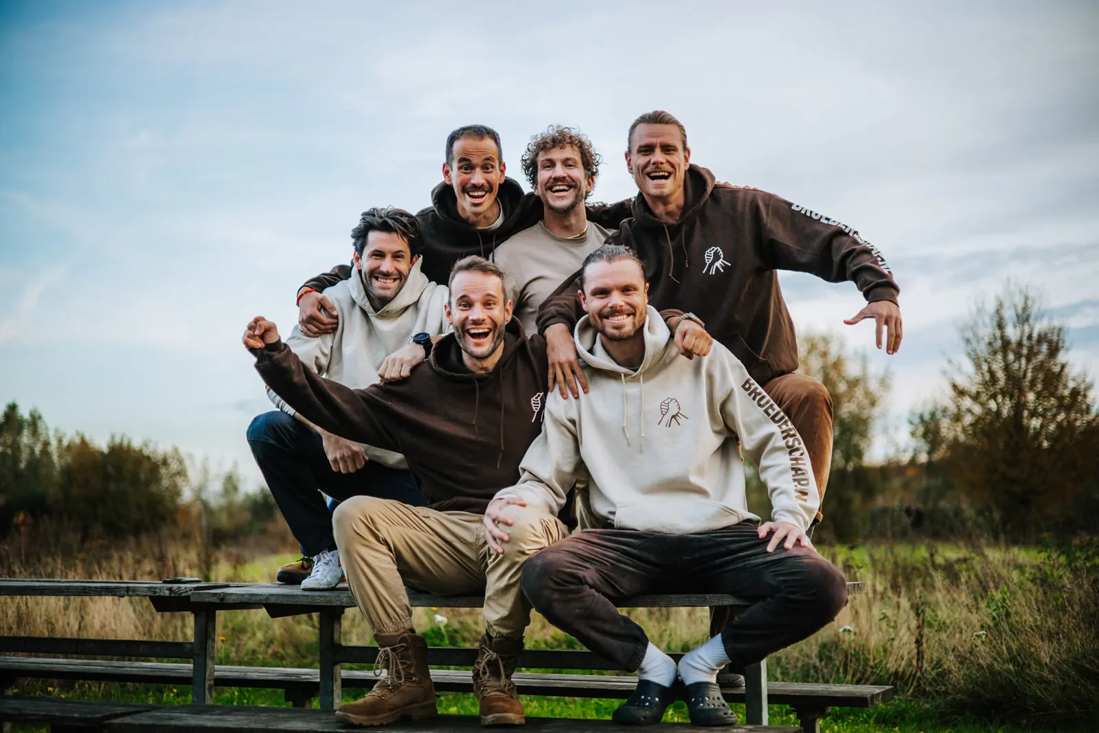 6 enthousiaste mannen die samen op een bank zitten en de camera inkijken