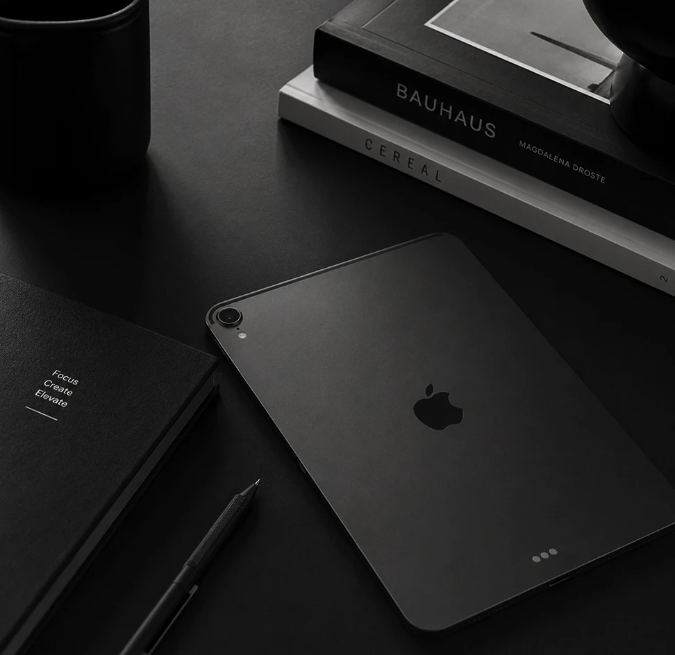 Design workspace flat-lay showing an iPad Pro, Bauhaus and Cereal design books, a notebook, and a pen on a dark surface