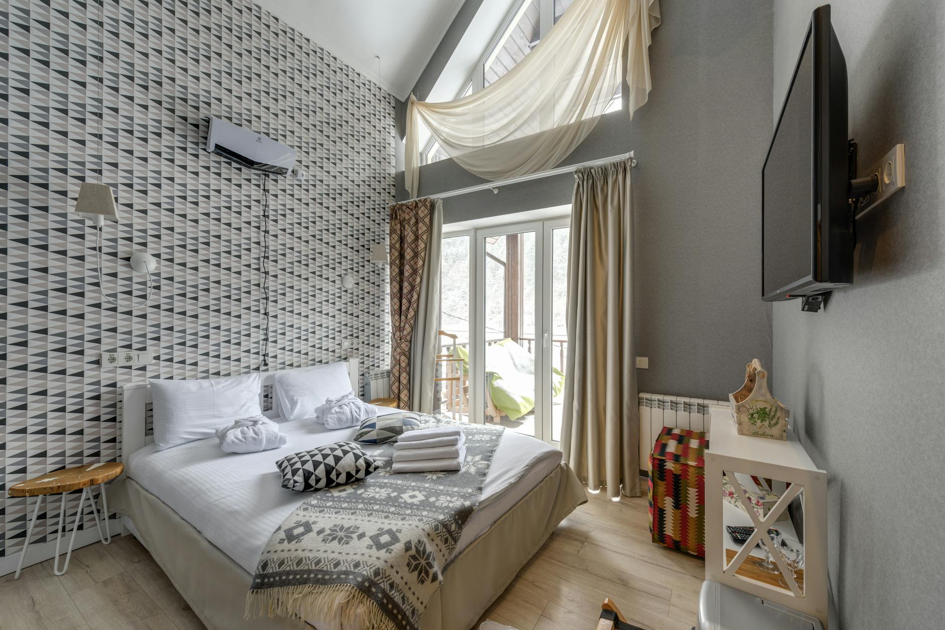 Stylish serviced apartment bedroom with geometric feature wall, double bed and wall-mounted TV