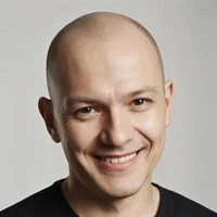 Smiling person in black t-shirt on light gray background, looking friendly and approachable.