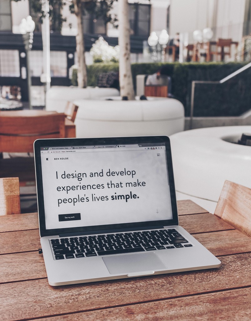 Laptop on an outdoor wooden table displaying a design portfolio homepage with the text “I design and develop experiences that make people’s lives simple.”