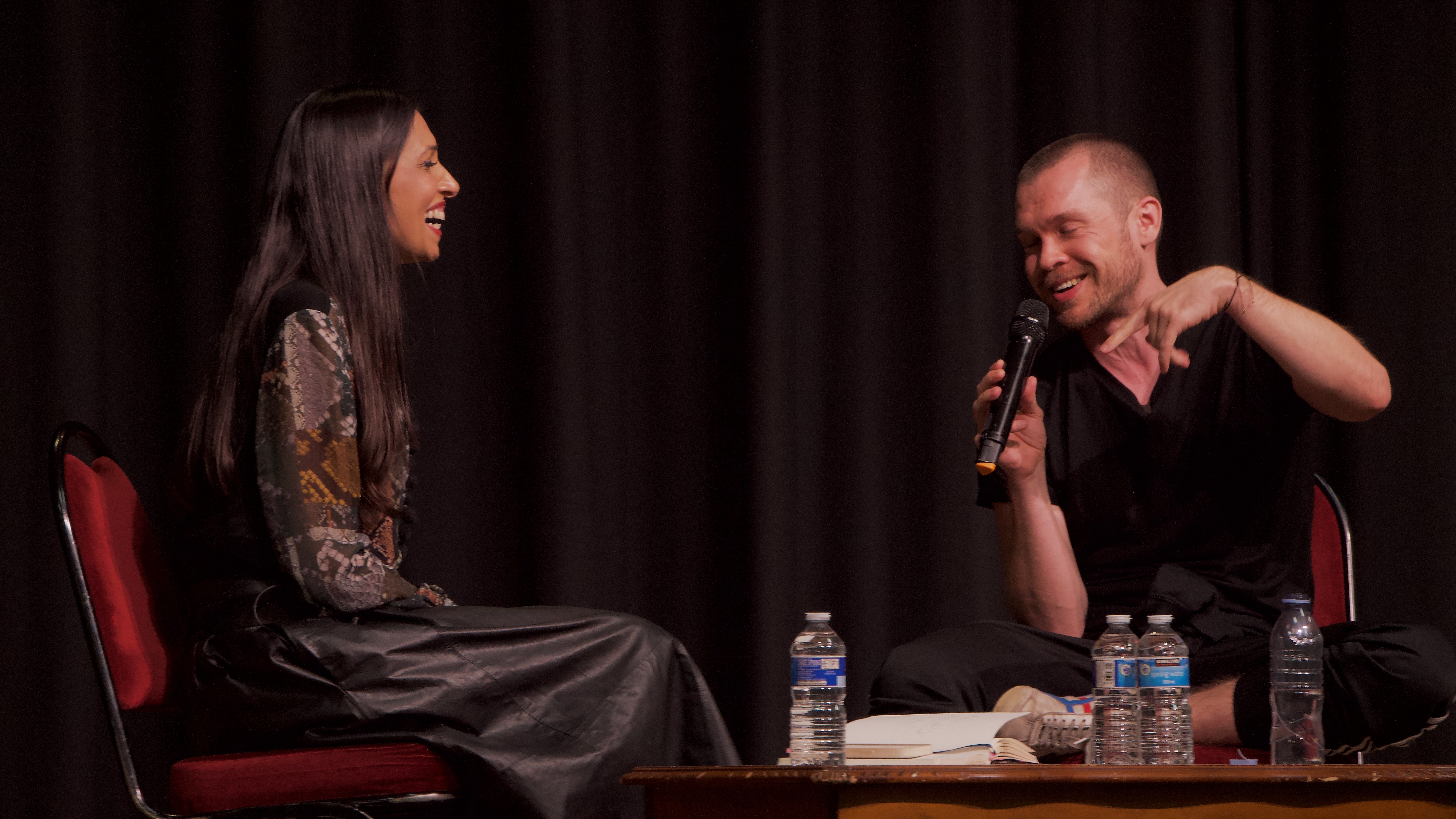 Faiza Shaheen in conversation with Gary Stevenson on stage with a microphone, laughing.