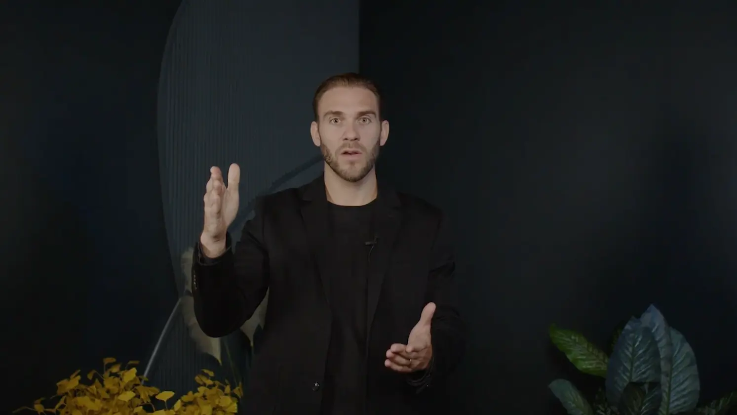 Homme face caméra dans un studio sombre, guidant un exercice de respiration avec des gestes de la main
