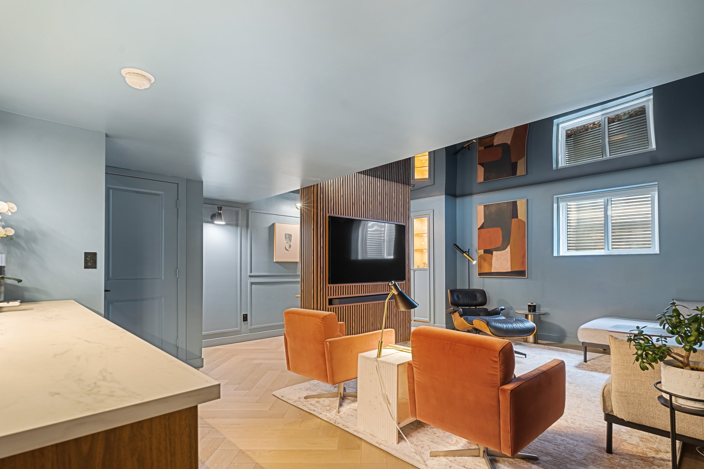 Crestmont basement finished: walnut slatted media wall, rust lounge chairs and herringbone oak floor