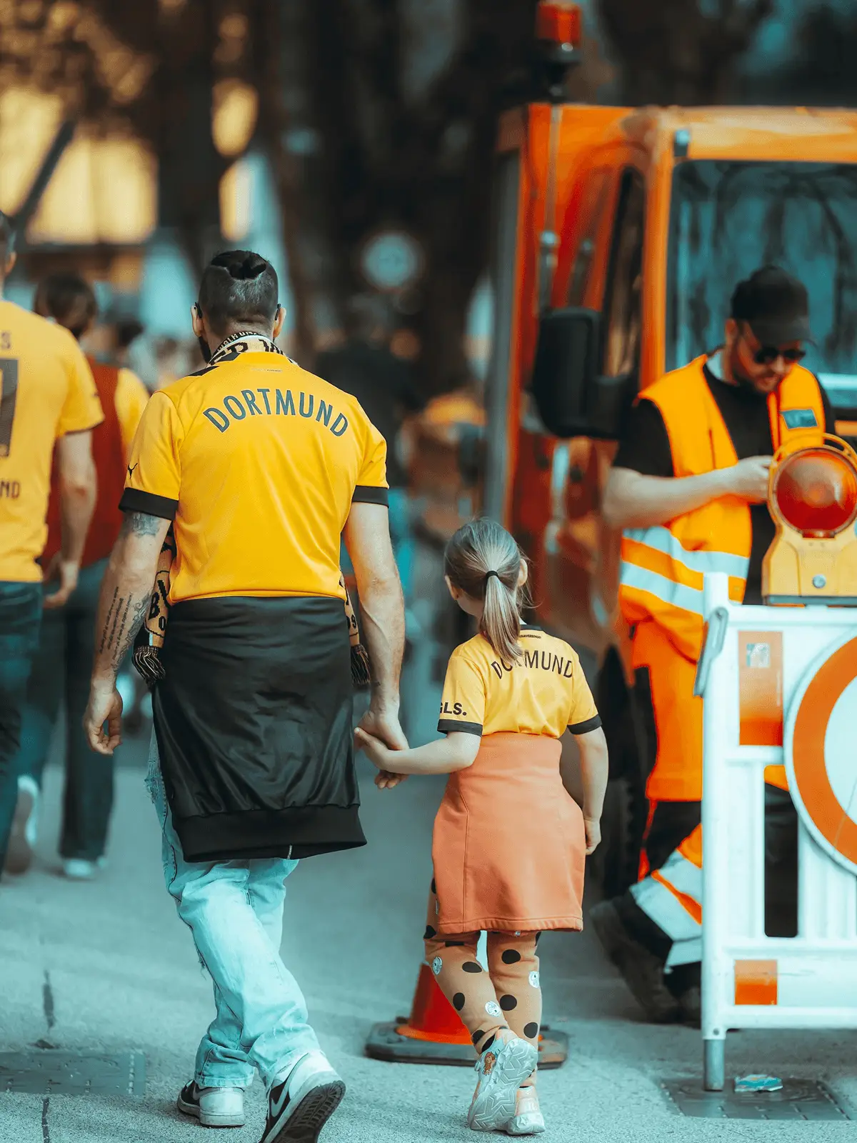 Fußballspieler mit Dortmund Trikot geht an der Straße und hält ein Mädchen in der Hand