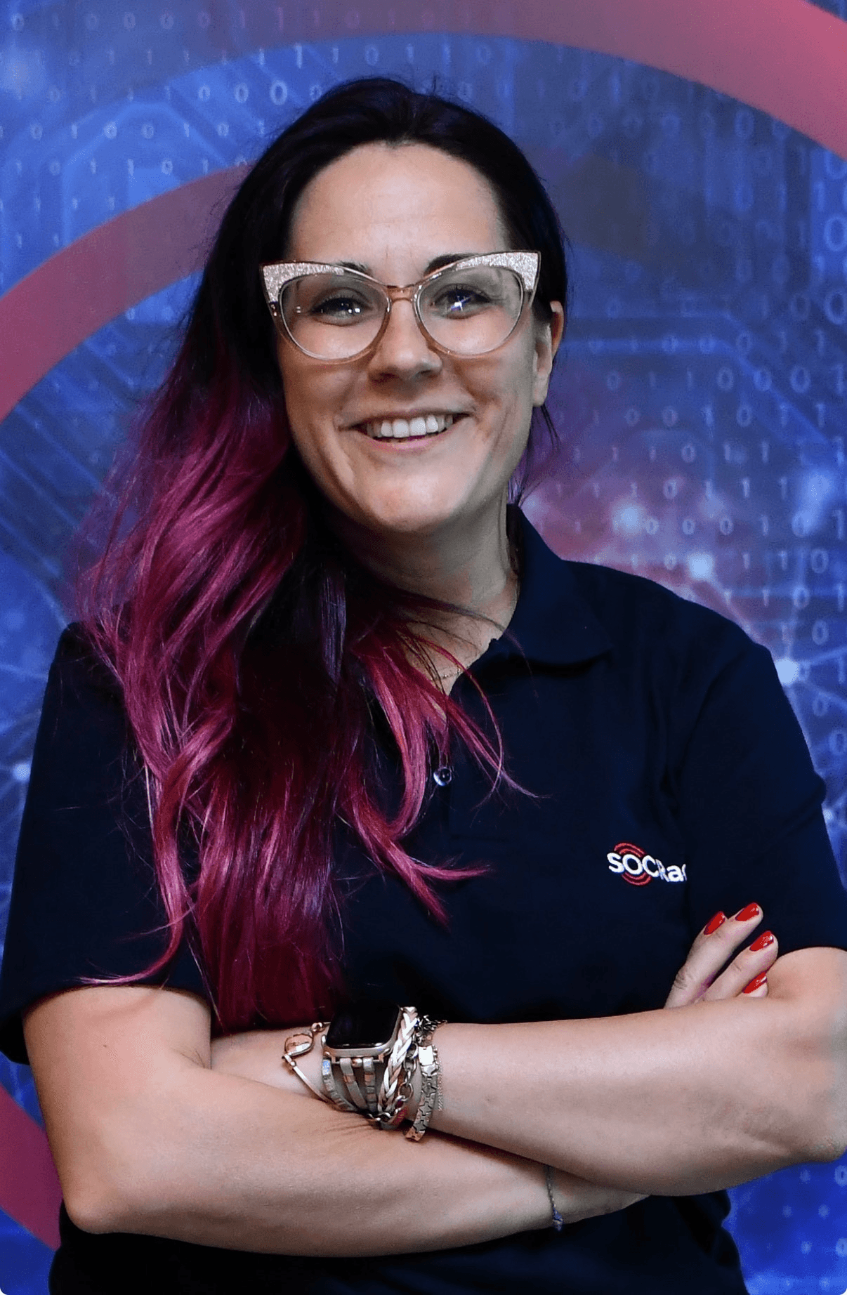 A smiling young woman in a pink blouse stands in an office setting, with soft lighting and a professional backdrop.
