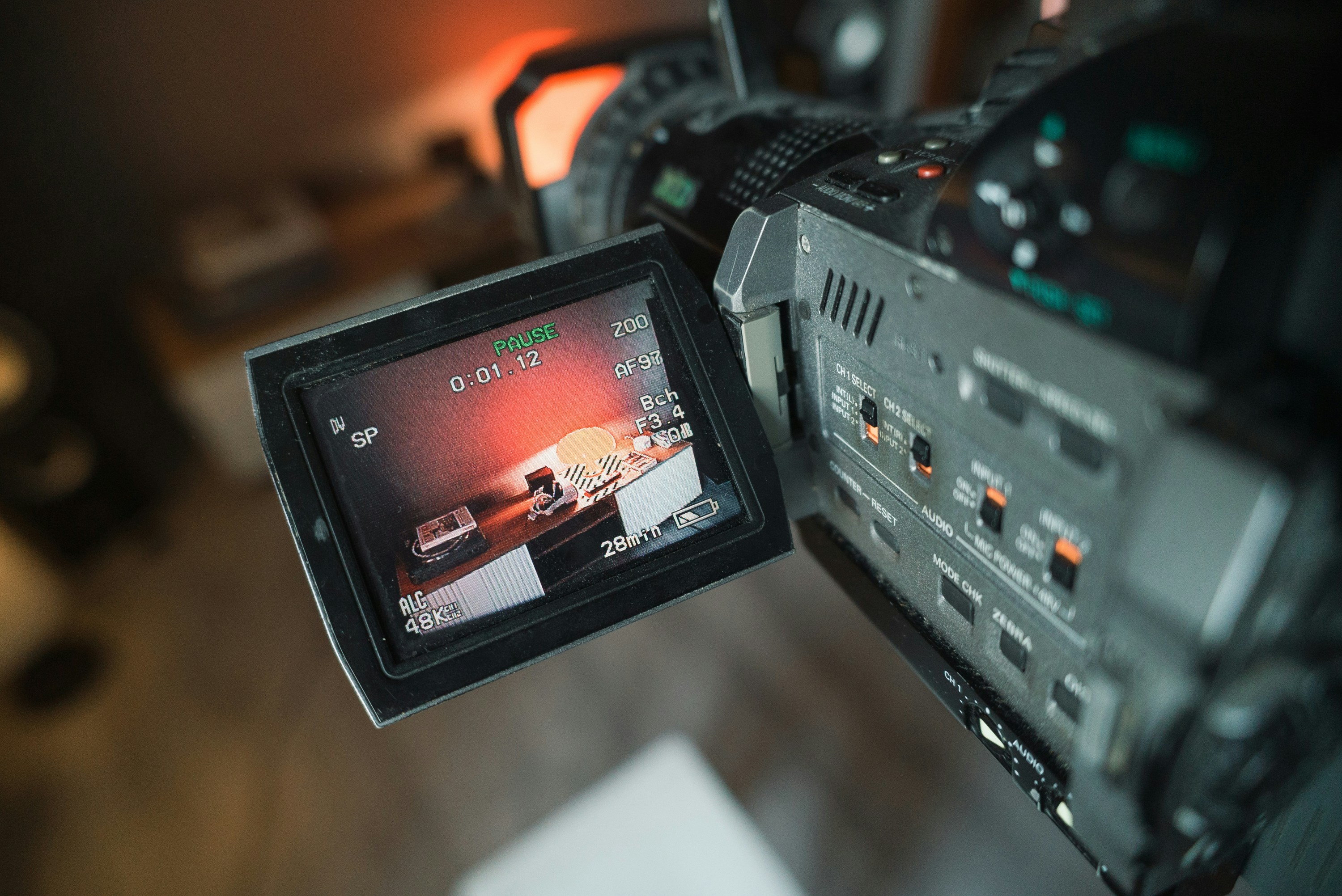 A woman stands beside an old projector, gazing at the camera. The scene is lit with teal and red hues, creating a mysterious and artistic atmosphere.