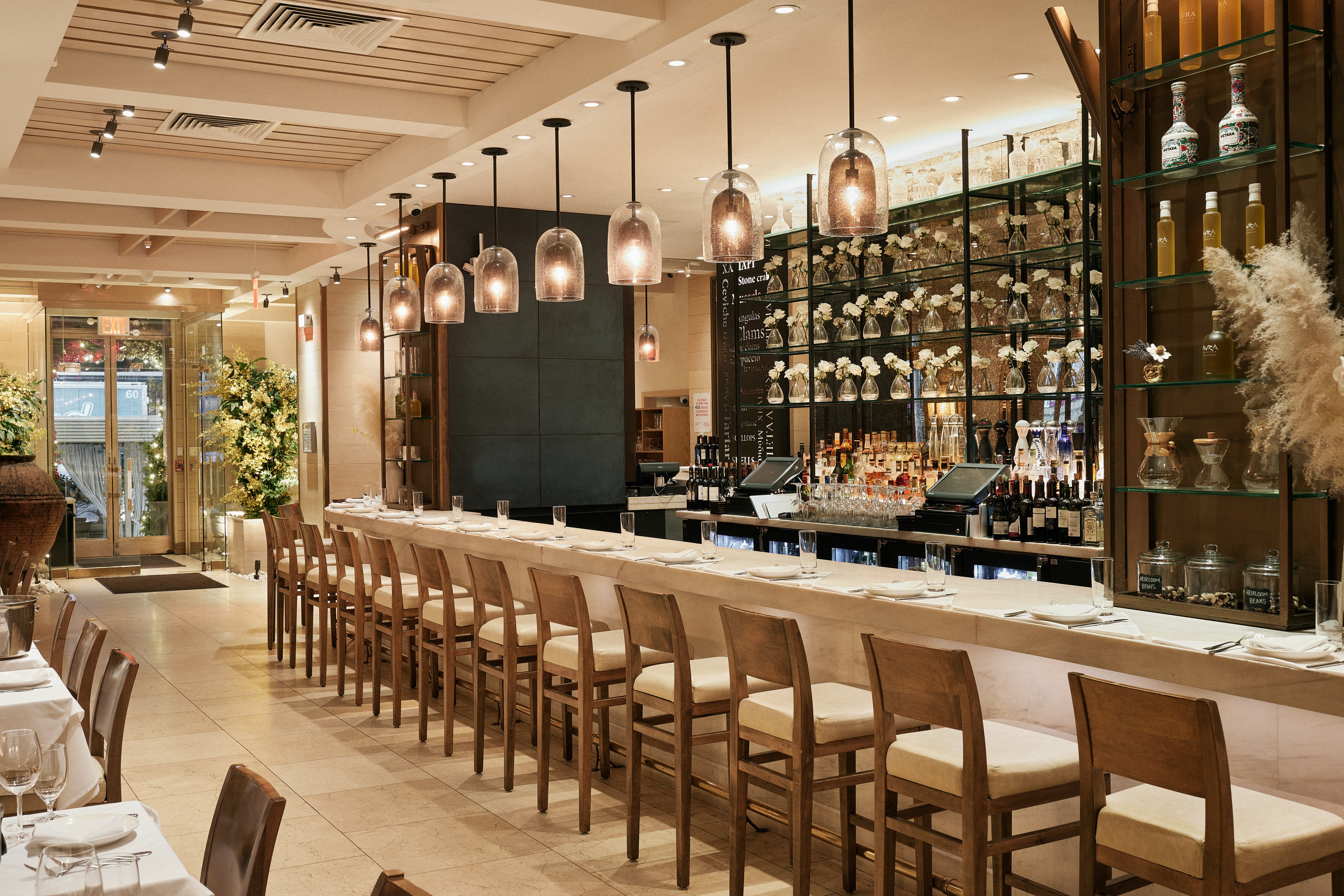 Modern restaurant interior featuring a sleek bar, wooden chairs, and decorative plants. Warm and inviting ambiance.