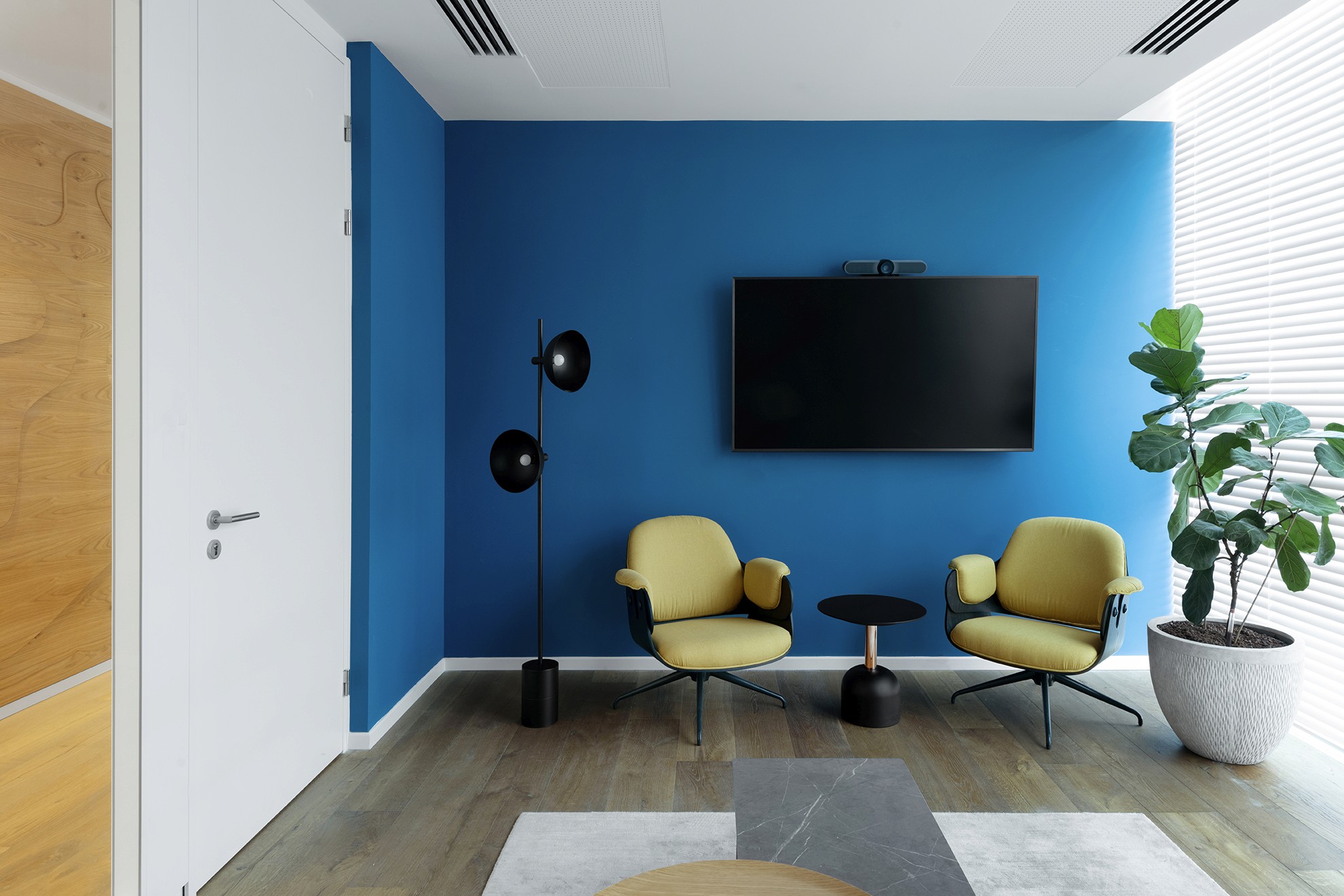 חדר מדיה/מנוחה: חדר אינטימי לשיחות לא-פורמליות, המשלב קיר כחול עמוק עם כורסאות בגוון חרדל ומסך למצגות או פנאי.