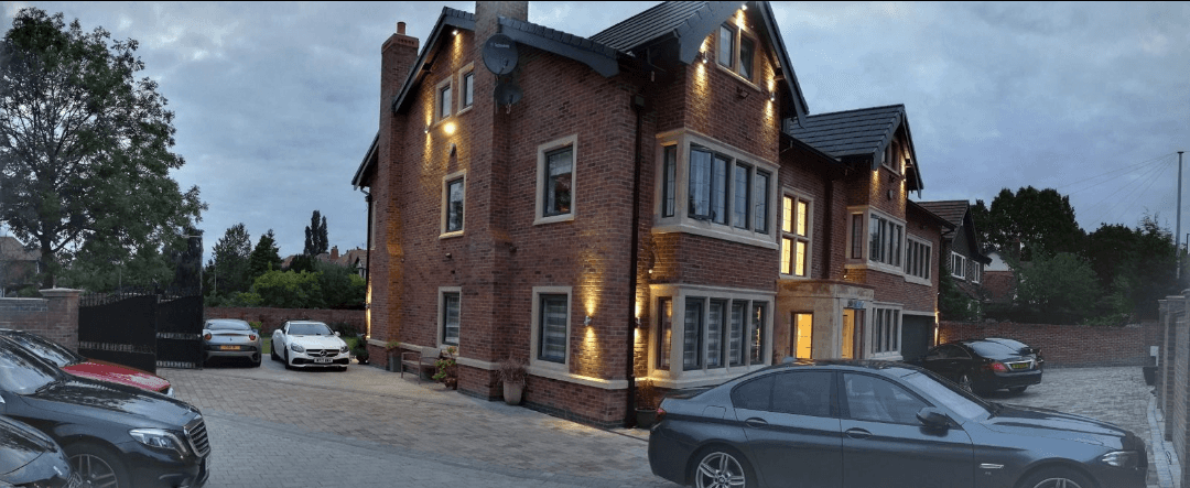 Panoramic view of a luxury six-bedroom house remodel with bespoke stonework, feature lighting, and spacious driveway.
