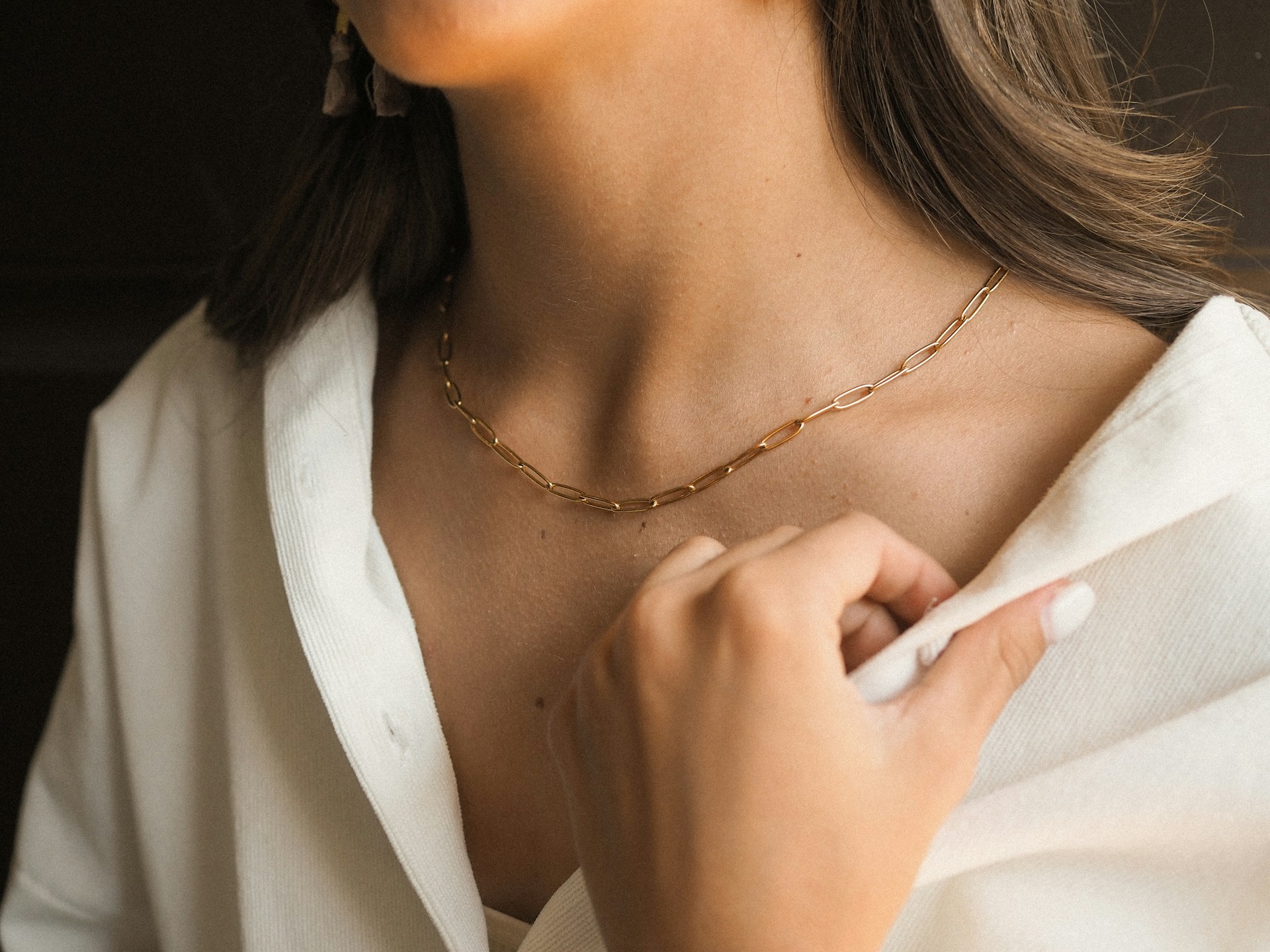 Close-up of a person wearing a delicate gold paperclip chain necklace paired with a white button-down shirt.