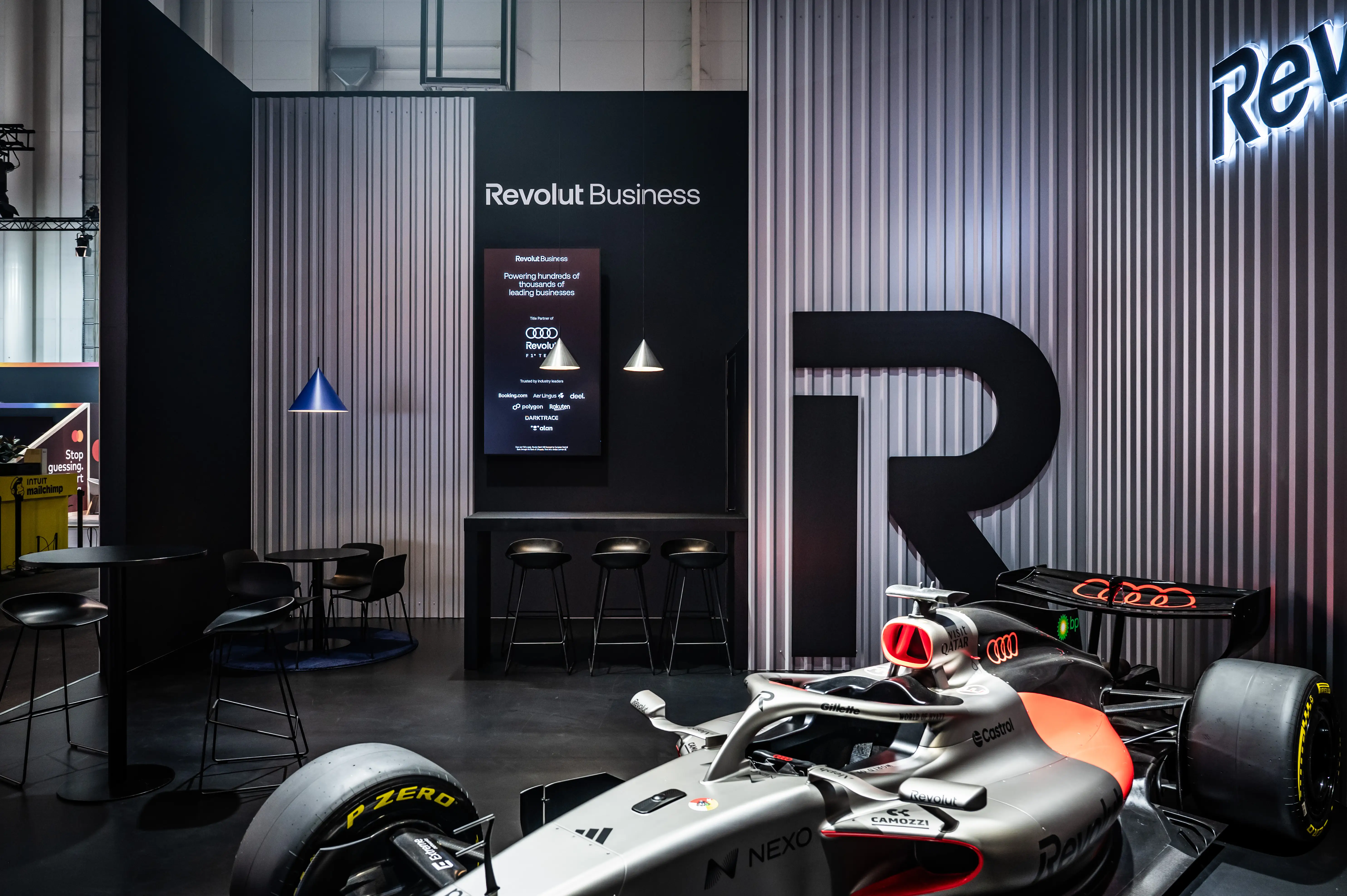 Formula 1 car beside the Revolut Business bar area with corrugated metal walls and large R logo.