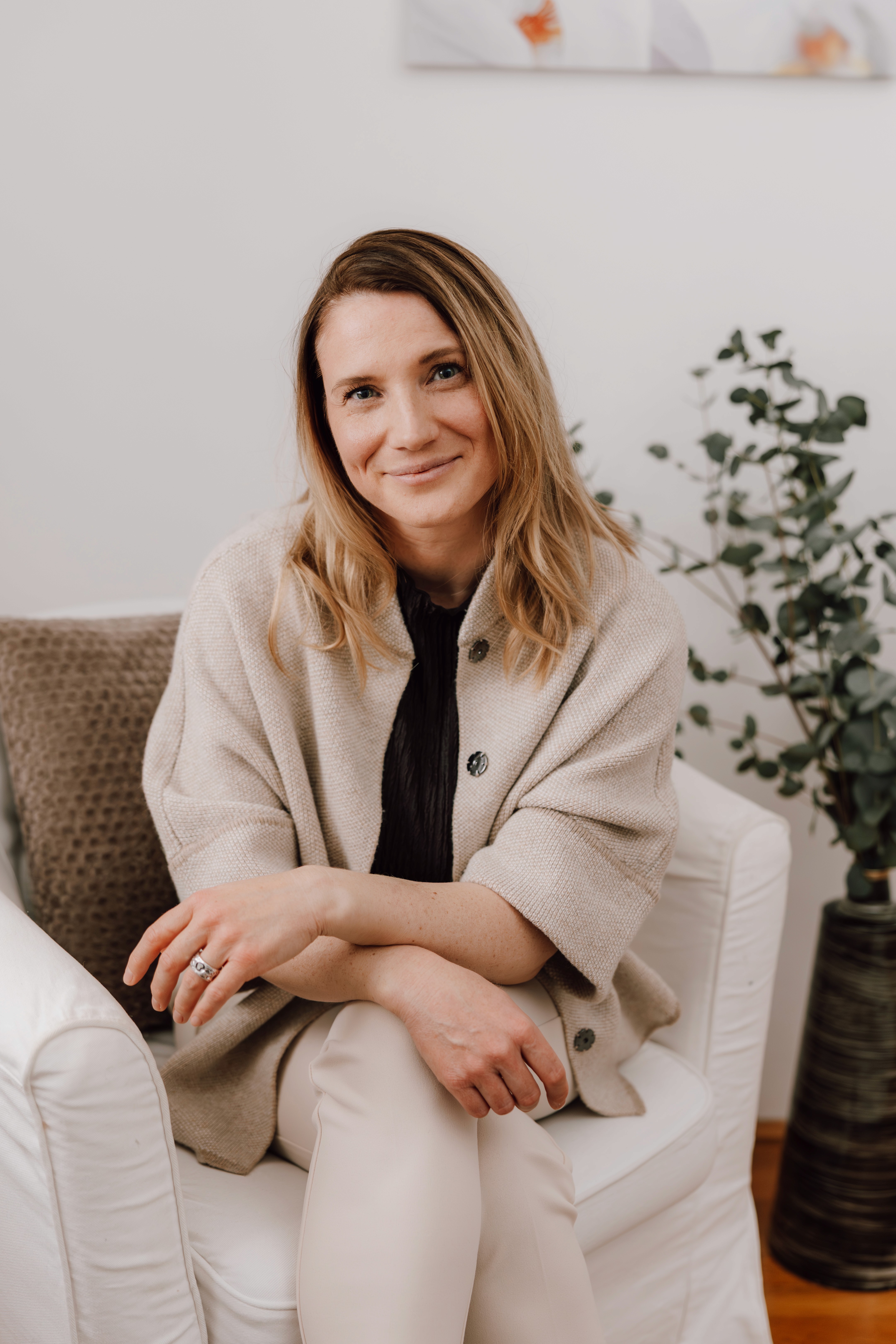 Smiling female therapist with short gray hair, wearing a brown top and a purple shawl, surrounded by a cozy background.