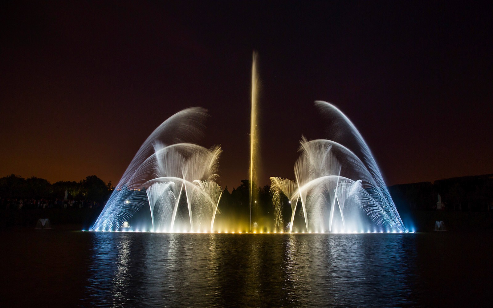 Espectáculo de fuentes por la noche en el Palacio de Versalles, con chorros de agua iluminados.