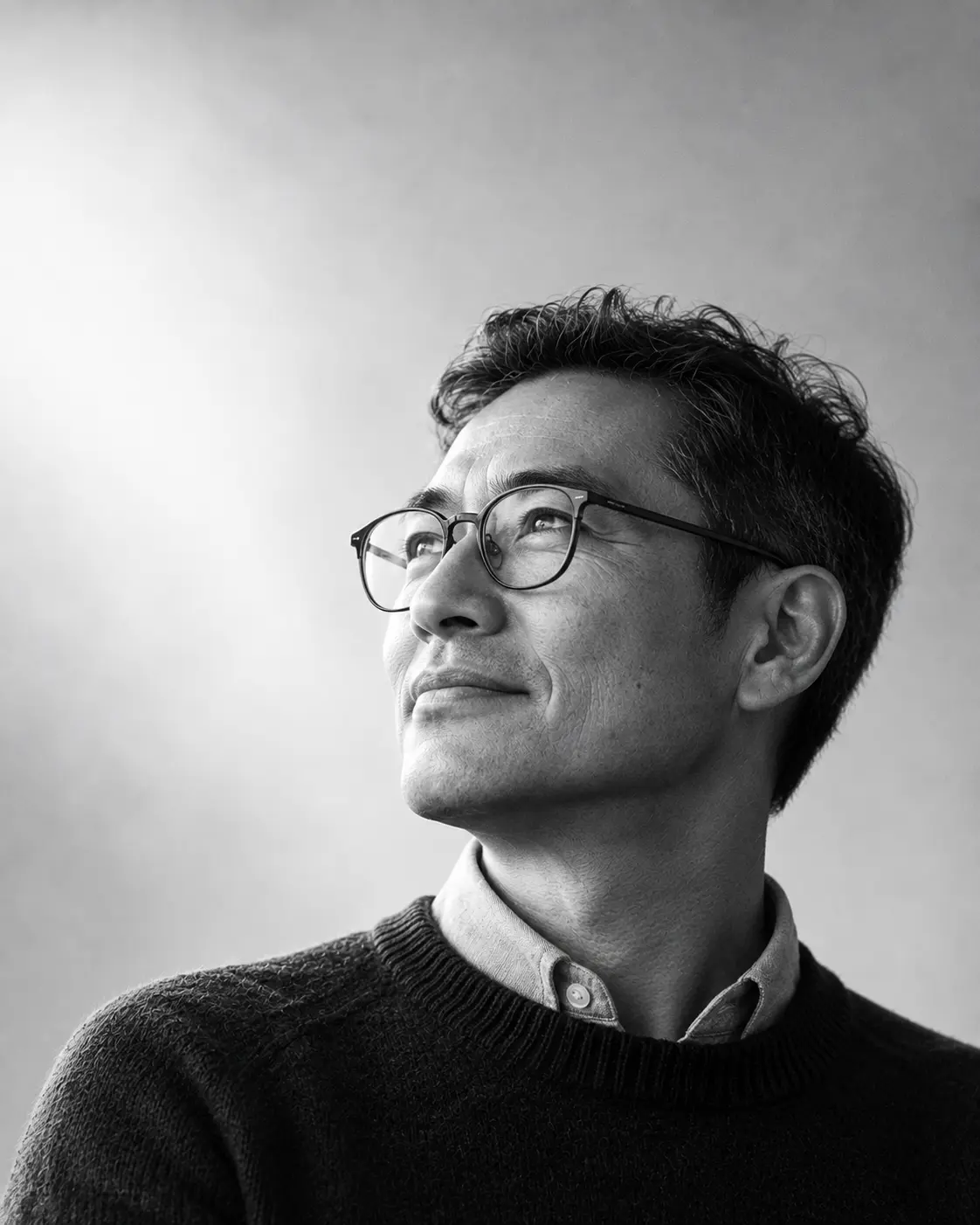 Kenji Arata, founding partner and head of tax, in thin-framed glasses and a dark sweater, looking up and to the left