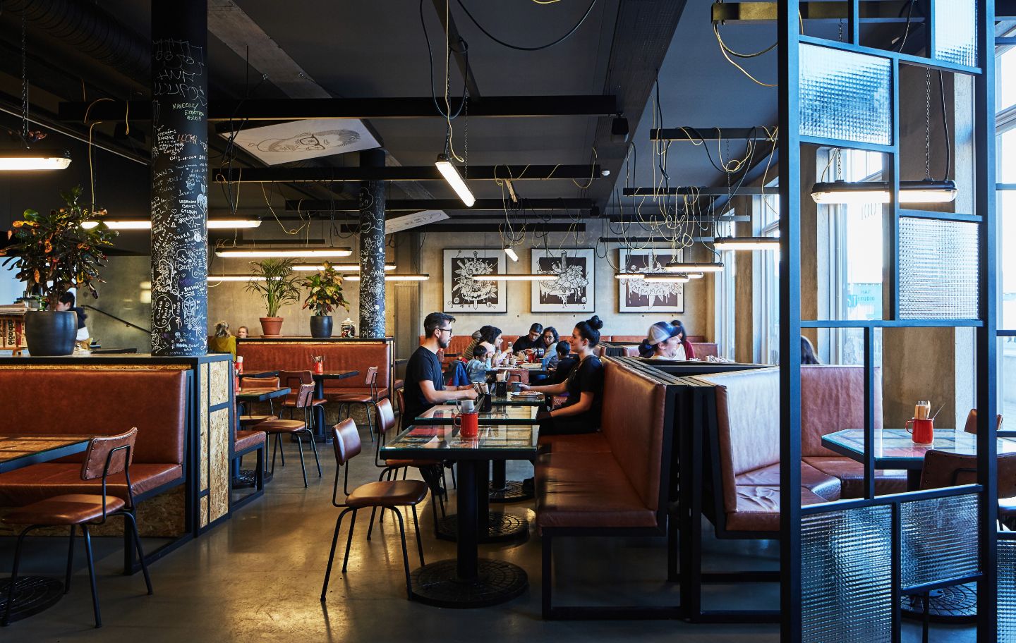 Guests dining inside Le Kock restaurant at Exeter Hotel in Reykjavík with modern industrial décor and comfortable booth seating.