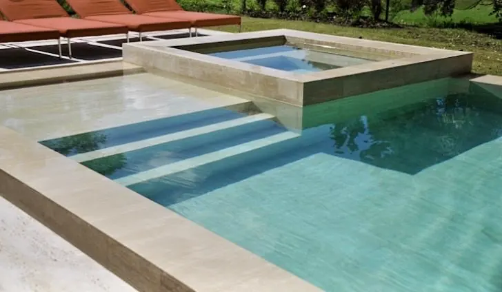 Diseño de piscina premium con escalones anchos y un exclusivo jacuzzi cuadrado elevado, construido con mármol travertino natural.
