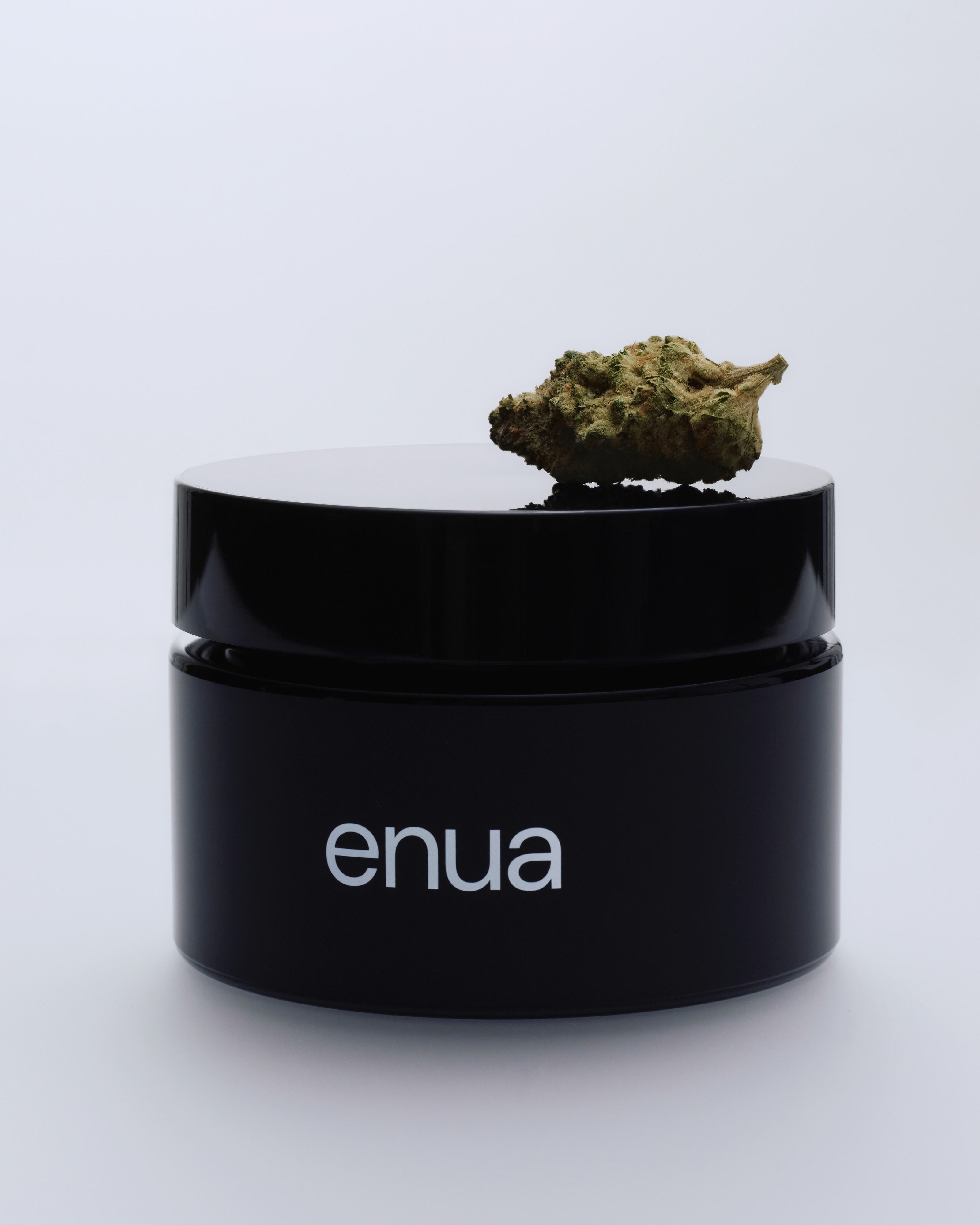 Eine enua Cannabisblüte der Sorte GellyPopper liegt auf einem schwarzen Aufbewahrungsglas.