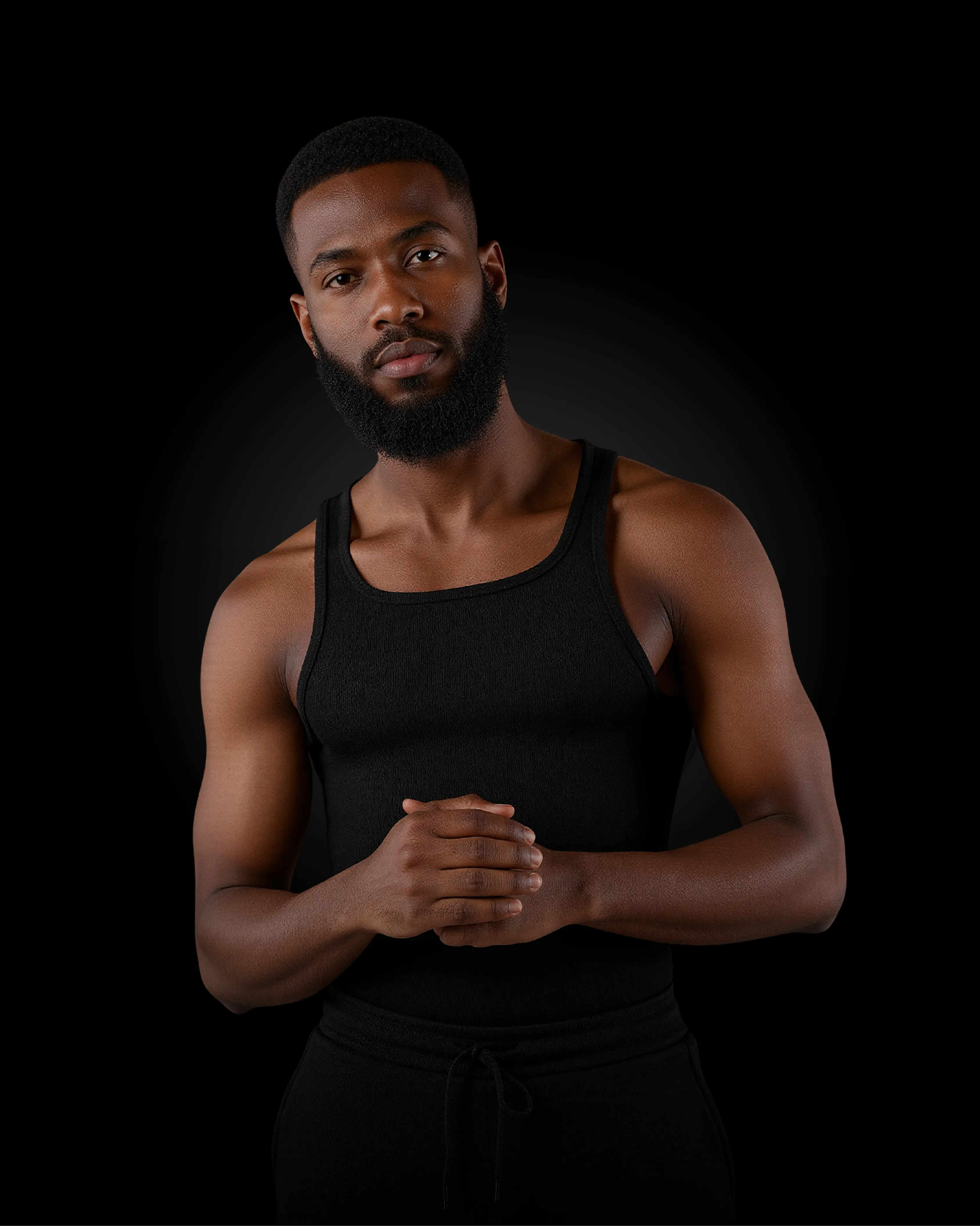 Handsome Black man with a beard wearing a black tank top, looking at the camera.
