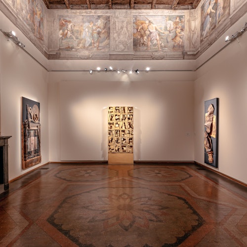 Una sala galleria con dipinti murali, due grandi opere d'arte incorniciate, un murale dettagliato sul soffitto e un pavimento con motivo in legno.