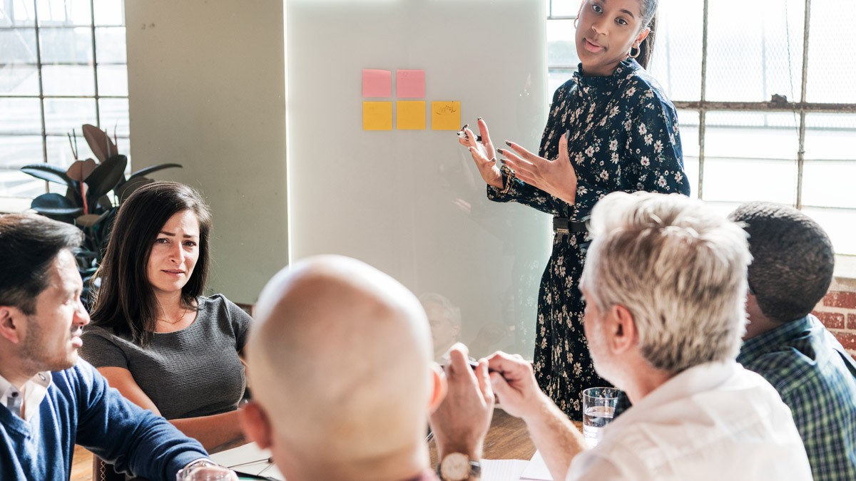 A facilitator speaking to a room of people while standing a front of a flipchart and taking notes