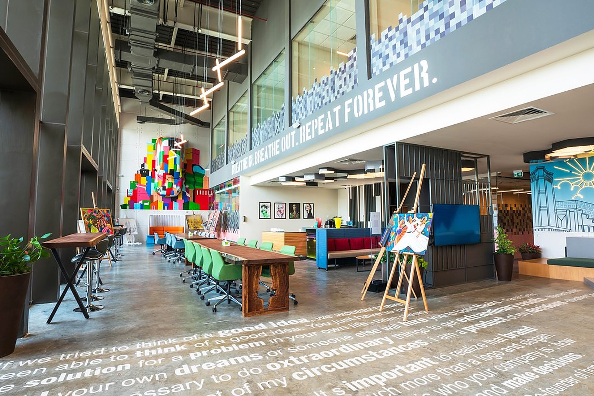 Le coworking du M7, à Msheireb, au cœur de Doha, avec sa grande table en bois, ses chaises vertes et sa fresque colorée, un bureau partagé pour les indépendants