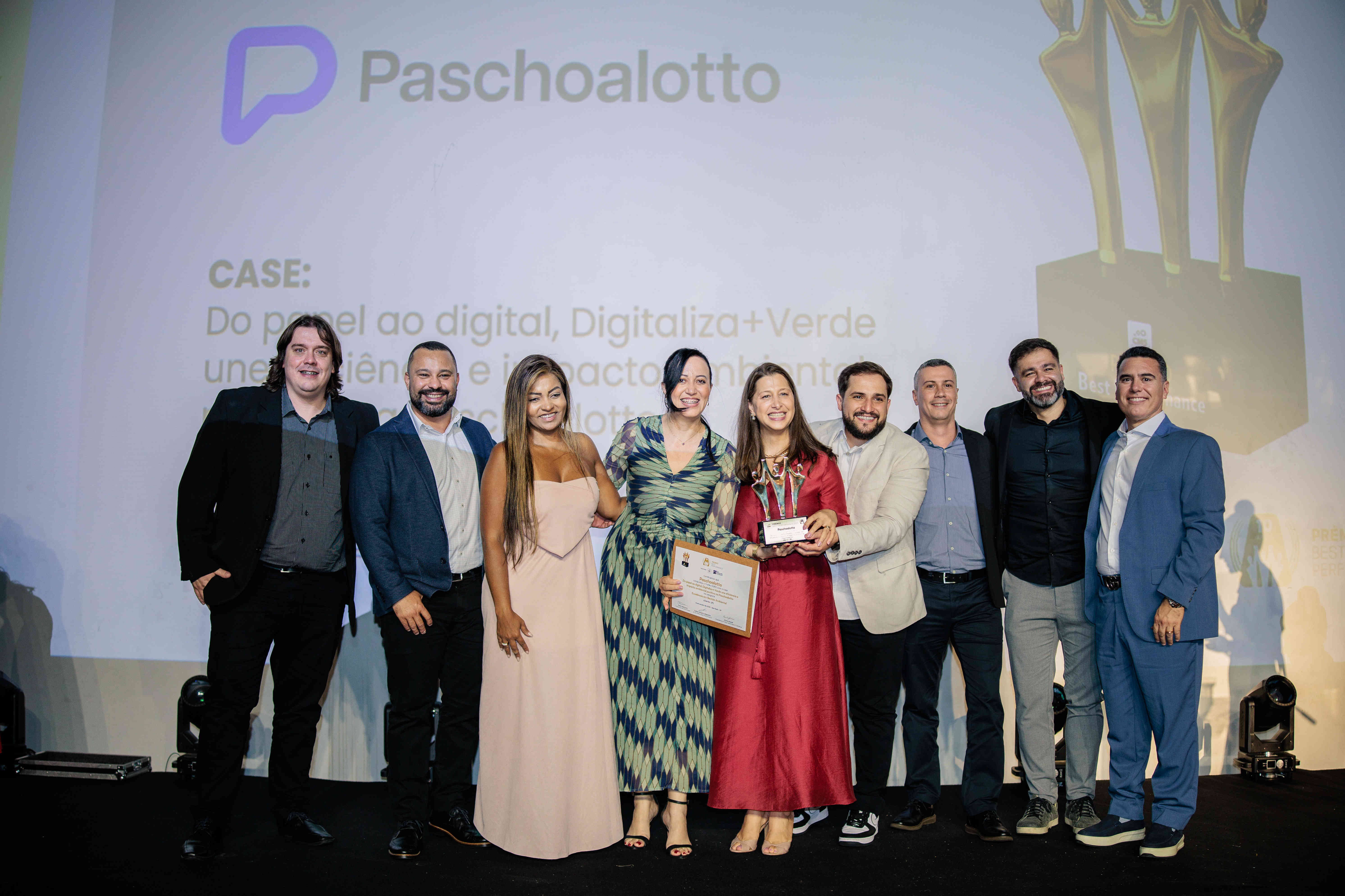 Executivos da Paschoalotto posando com troféu ouro e certificado no palco do Prêmio Best Performance 2025