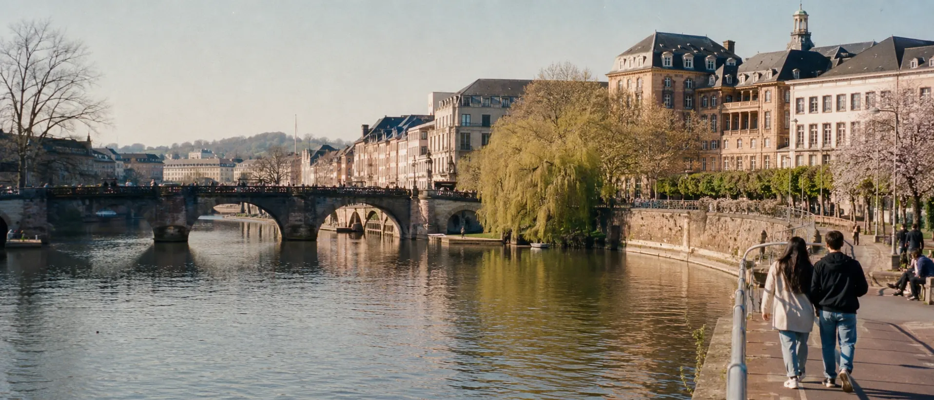 Saarbrücker Saarufer mit Brücke, Spaziergängern und barocken Fassaden im Morgenlicht