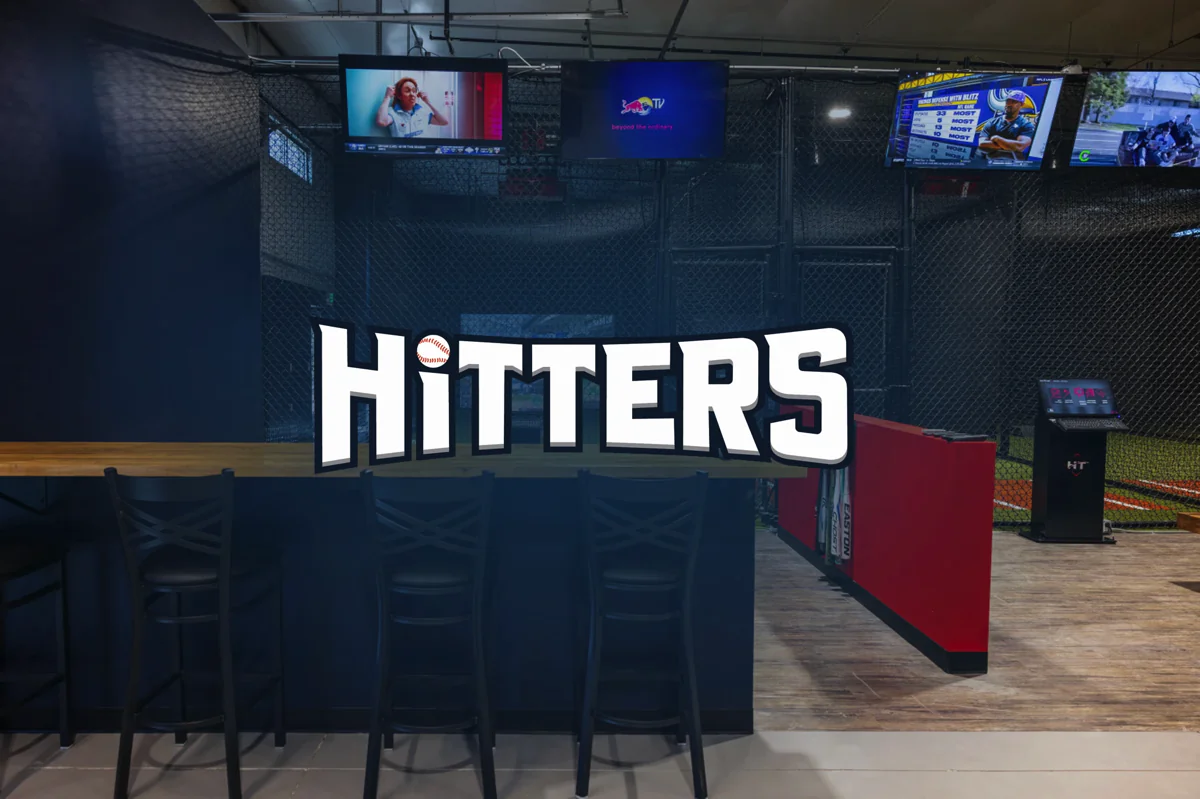 Hitters Liberty Lake logo over a HitTrax Suite batting cage lounge with TVs and seating.