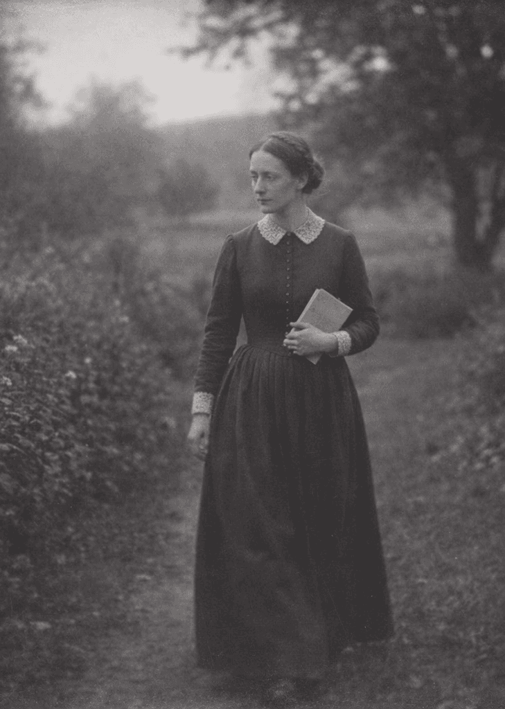 A 19th century wooman walking in the gardens, holding a book.