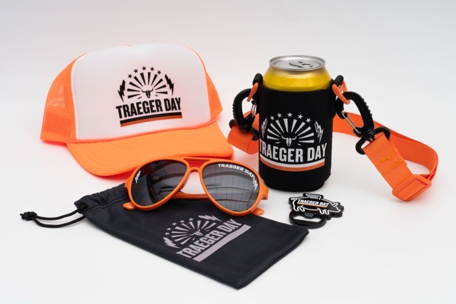 An image of all the products included in the Traeger Day kit. These products include a white and orange hat, orange glasses, a drink insulator, and a bottle opener. All the products are photographed against a white surface.