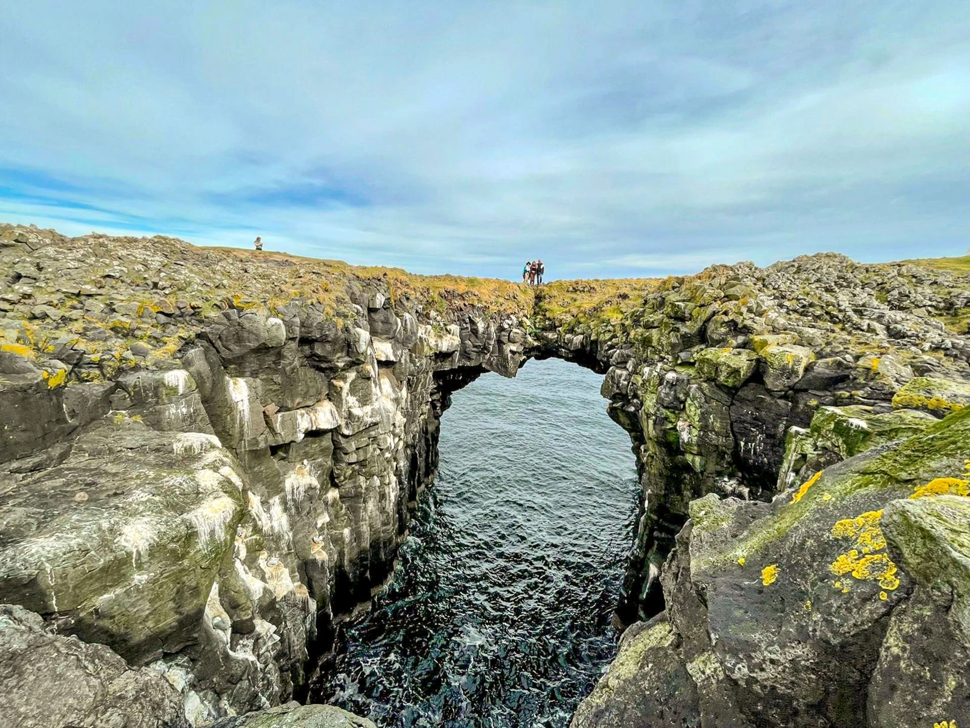 One bikerider riding a trail on a lava field with a small pond in foreground