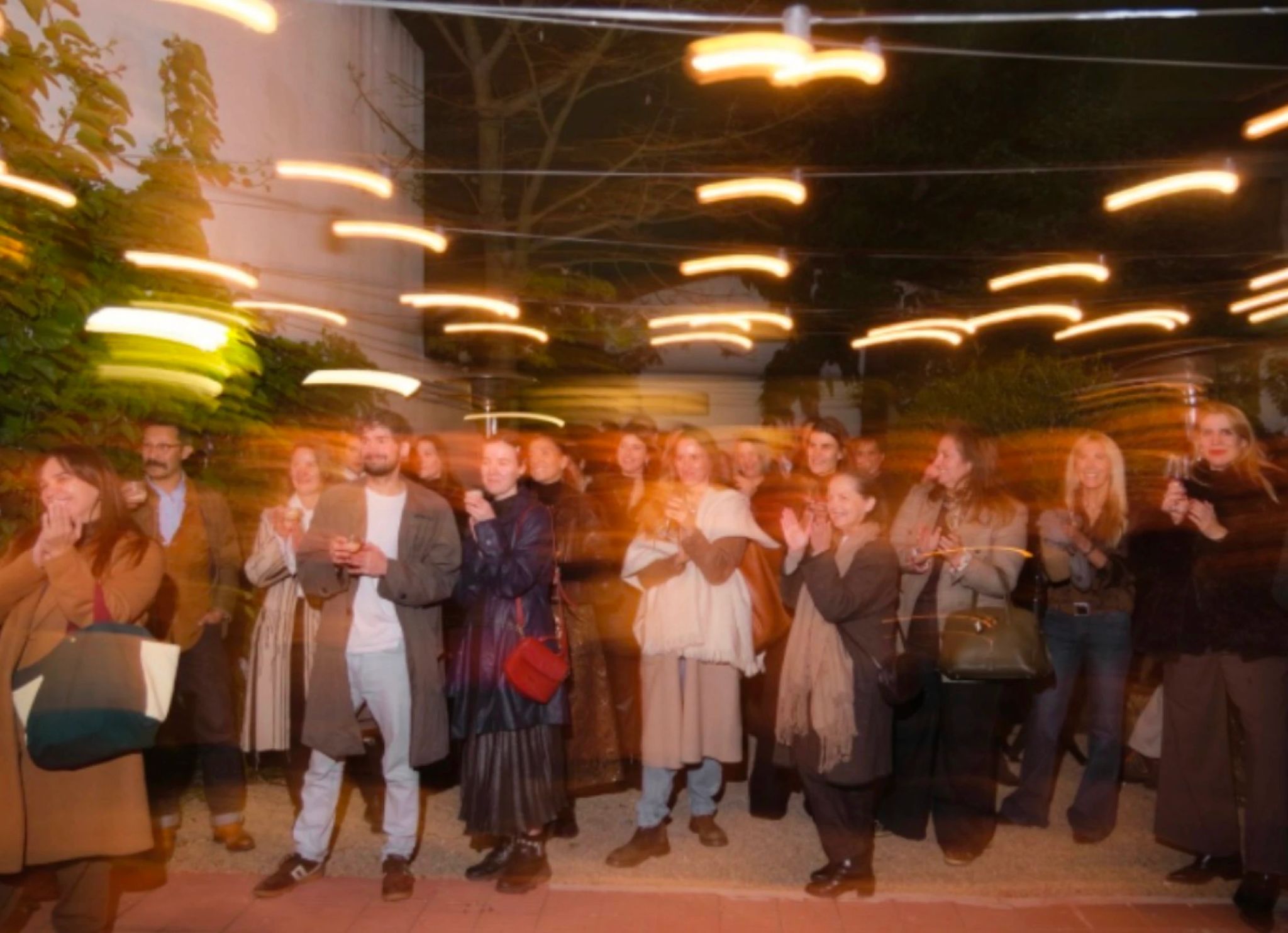 Grupo de personas aplaudiendo durante un evento nocturno con luces en movimiento.