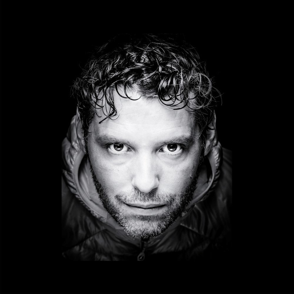 Thomas Biasotto Intense black-and-white close-up portrait of a man in a hooded jacket.