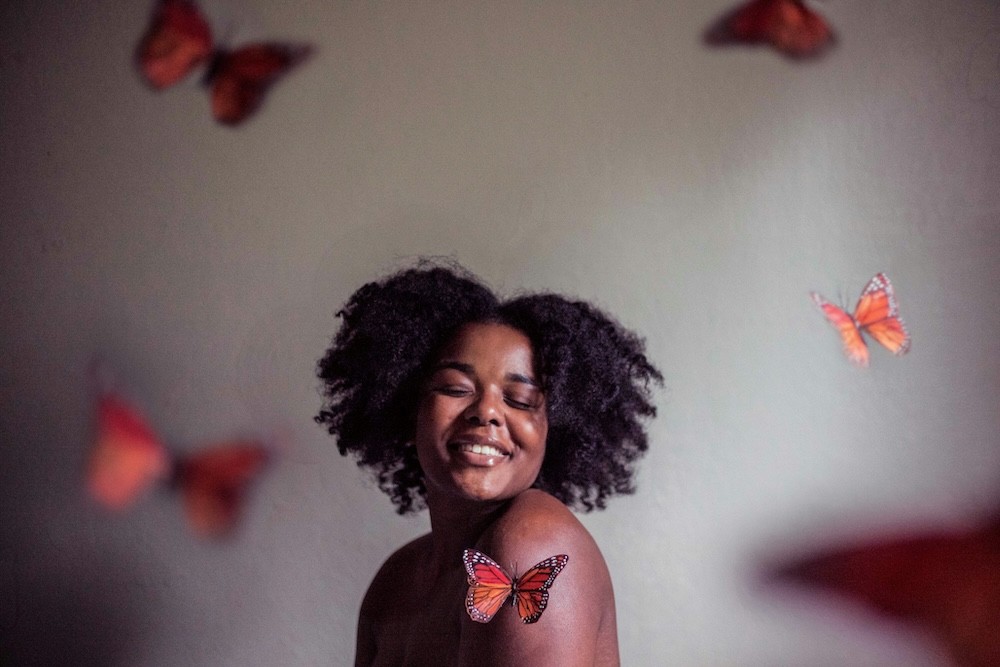 a smilling woman with curly hair surrounded by butterlies