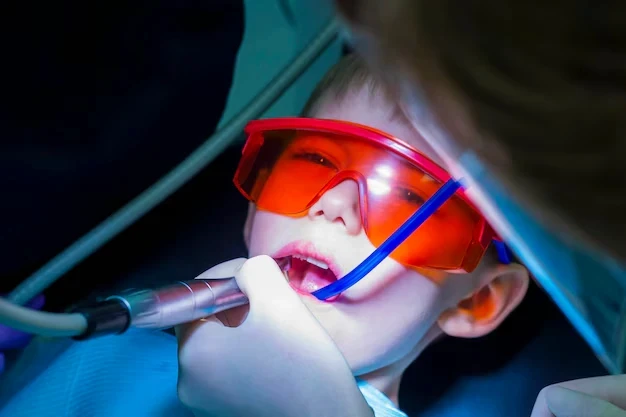 Young patient wearing protective glasses receiving laser dental treatment.