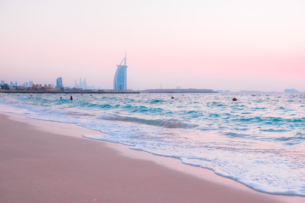 A view of the sunset over the beach with waves in the foreground and Burj Al Arab in the distance. 