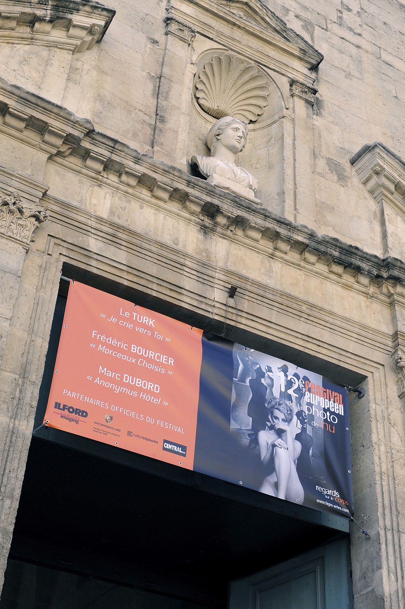 Vue intérieure d’un conteneur d’exposition présentant les portraits en noir et blanc de Frédéric Bourcier, éclairés par des néons au plafond.