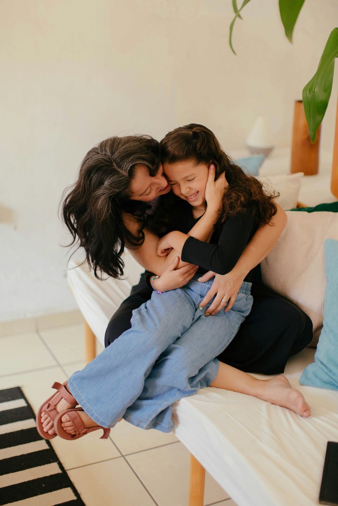 A mother and daughter share a heartfelt embrace, sitting on a couch in a cozy home setting, exuding warmth and familial love.