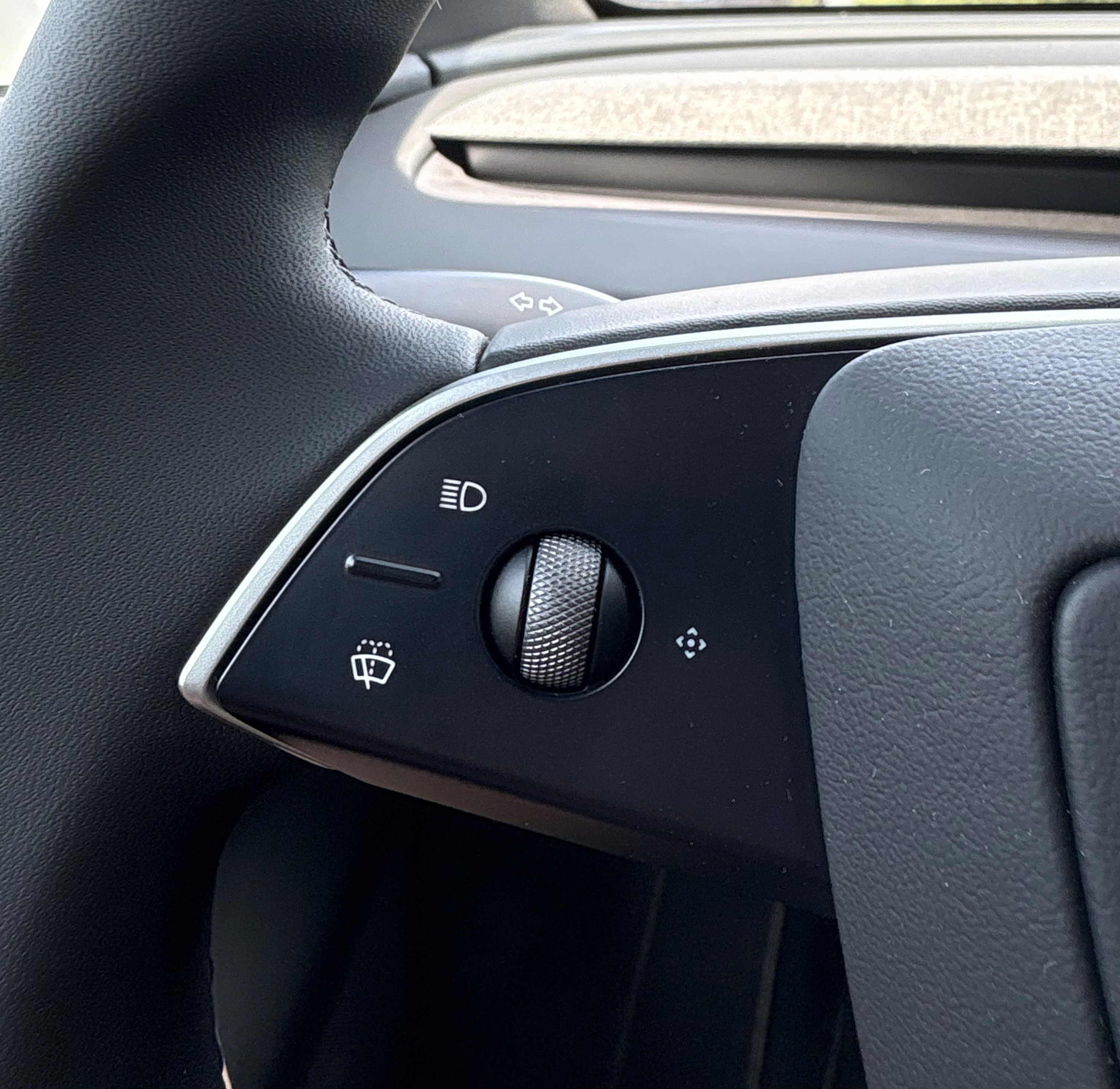 Close-up view of Tesla Model Y's steering wheel showcasing the headlight control switch, including options for automatic lights and fog lights, set in a sleek black interior.