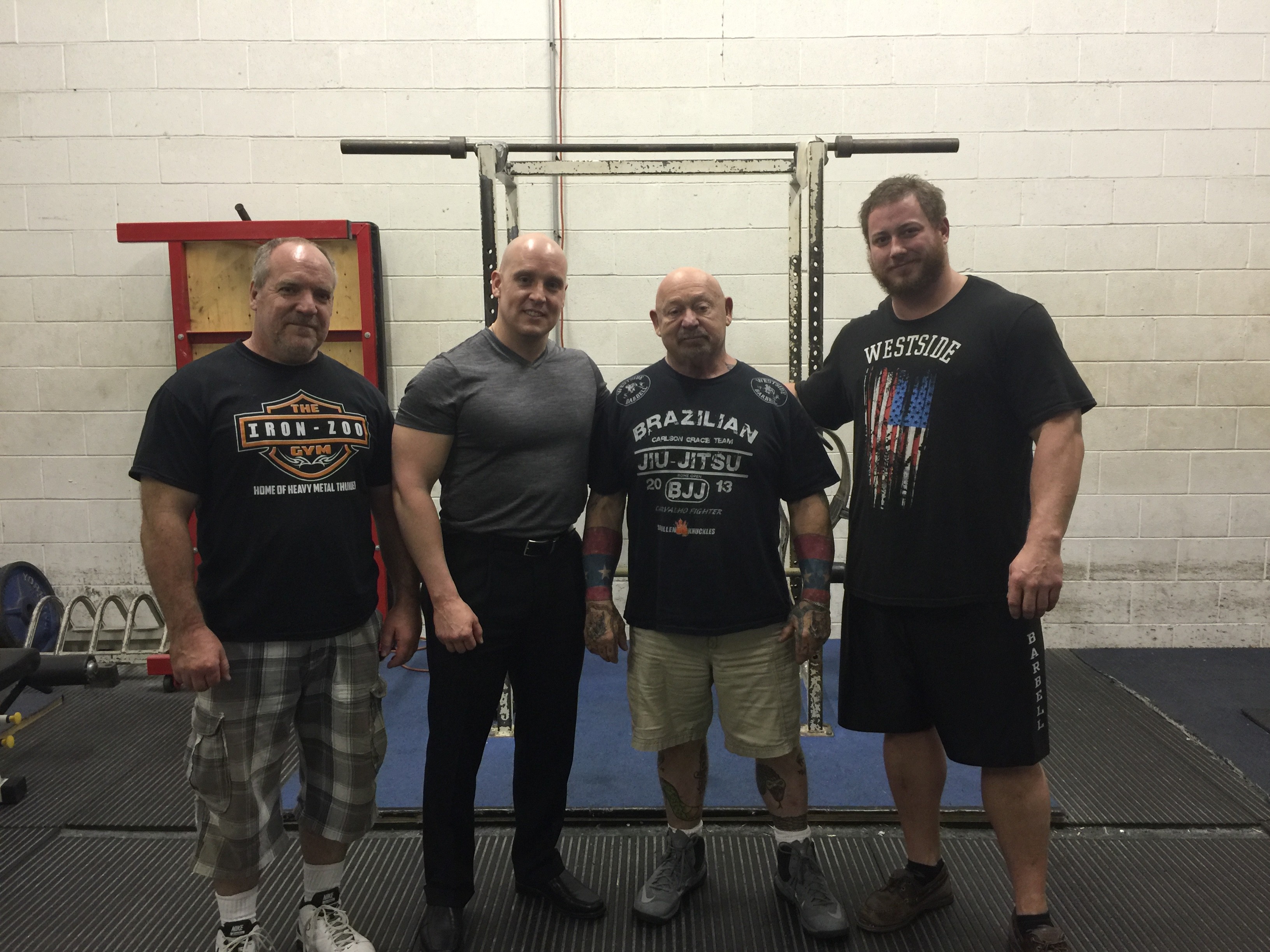 Four men standing in front of a power rack, one wearing a Westside Barbell shirt