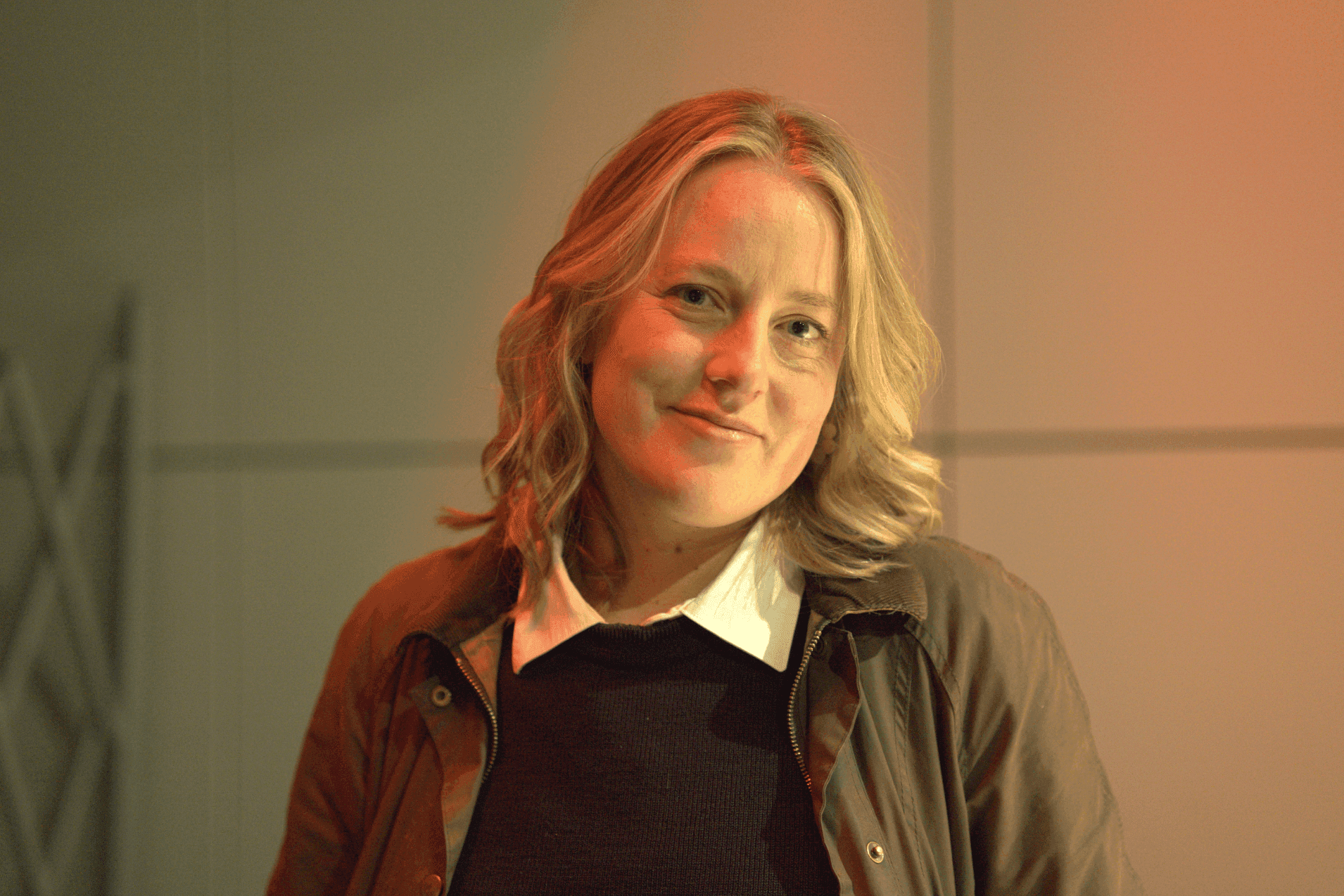 A smiling Helen Osborne, a head of the agency, with shoulder-length blonde hair, wearing a dark outfit, is standing against a softly lit background.