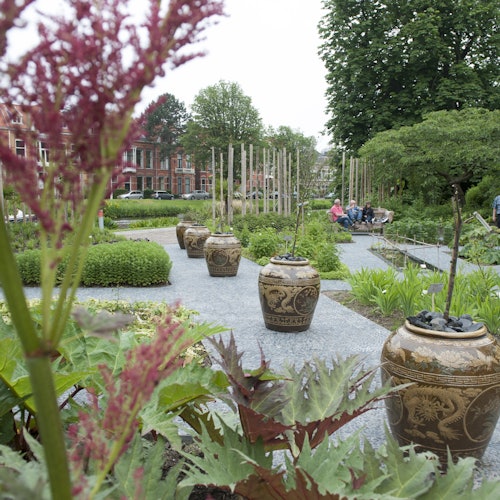 一個風景如畫的花園,裡面有裝飾性的花盆,郁郁蔥蔥的綠意,以及坐在長椅上的人們。紅磚建築在背景中可見。