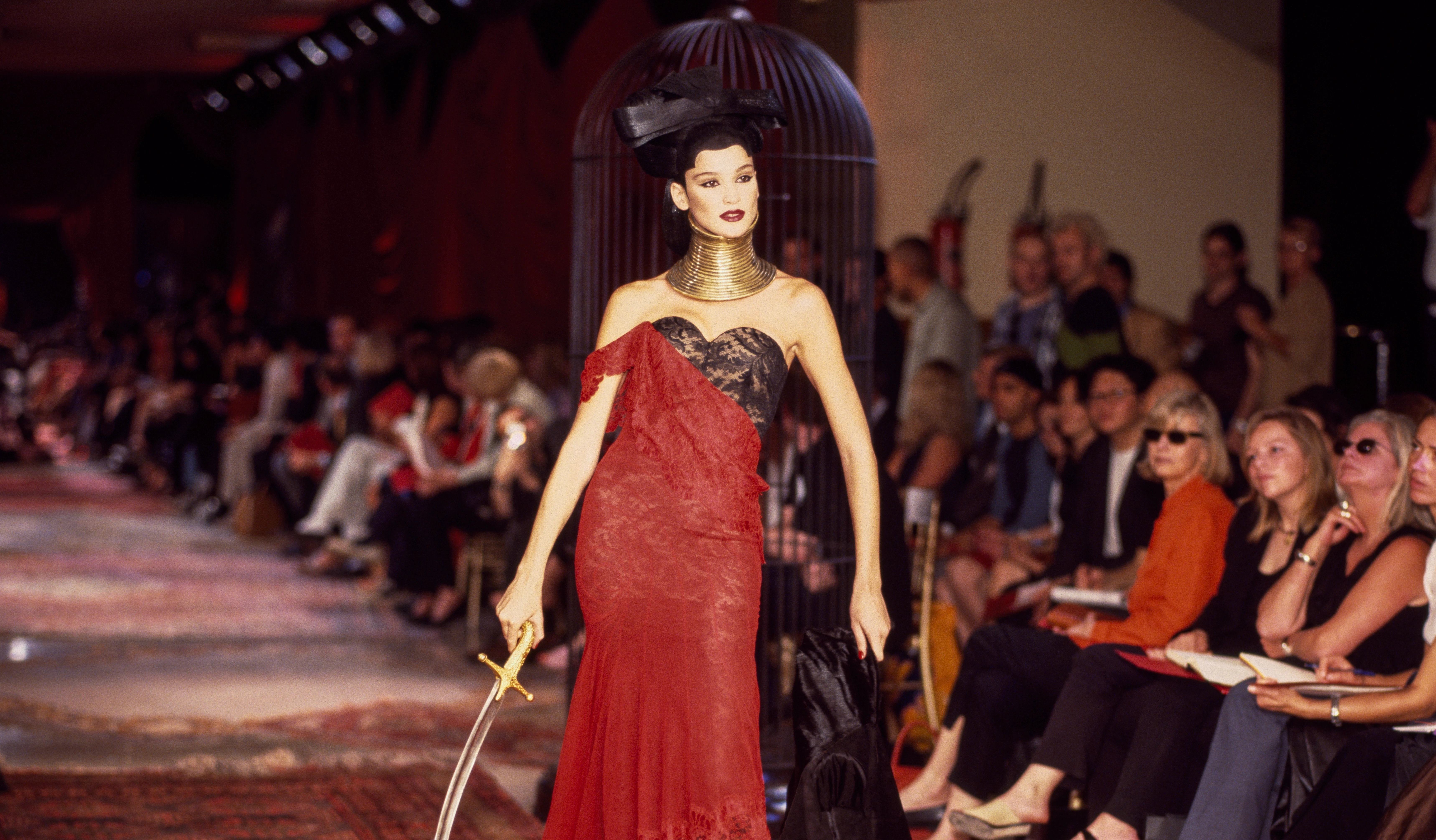 Runway model wearing a tall, structured gold coiled neckpiece designed by Shaun Leane for Givenchy haute couture by Alexander McQueen, styled with a red lace gown.