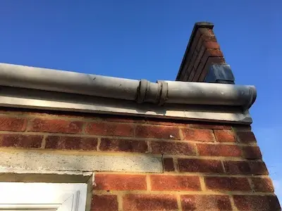 Close-up of a brick wall with lead flashing and guttering on the edge of a pitched roof in the UK.