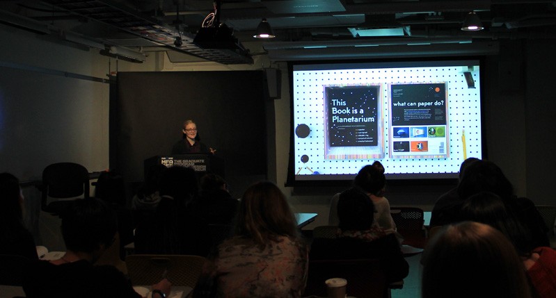 a woman presenting her project from a stand in front of people