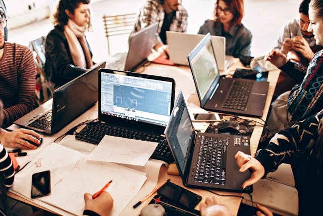 People seated at a large desk working on laptops