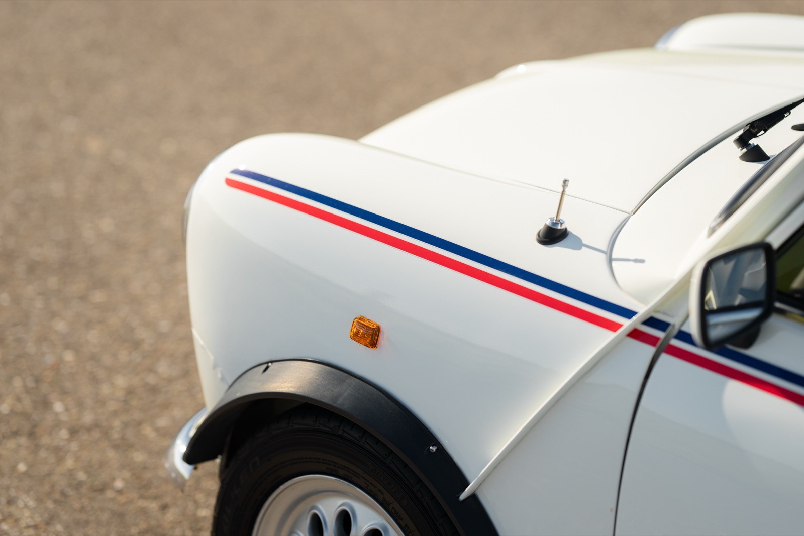 Close-up of a white car's fender with a red stripe, showing the wheel and part of the car body.